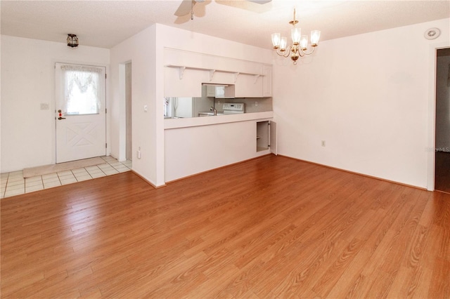 unfurnished living room featuring light wood-style flooring and ceiling fan with notable chandelier