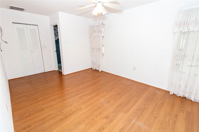 unfurnished bedroom featuring light wood-type flooring, a ceiling fan, visible vents, and a closet