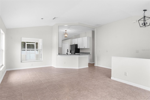 unfurnished living room featuring a chandelier, plenty of natural light, vaulted ceiling, and baseboards