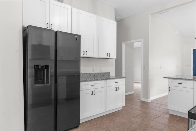 kitchen with light stone counters, fridge with ice dispenser, white cabinetry, and baseboards