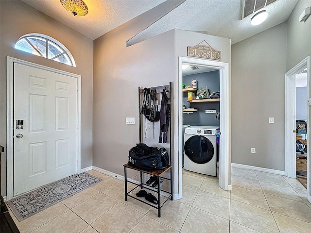 foyer with light tile patterned floors, a textured ceiling, washer / dryer, and baseboards