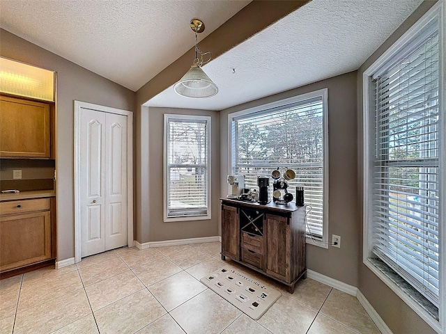 interior space featuring lofted ceiling, a textured ceiling, baseboards, and light tile patterned floors