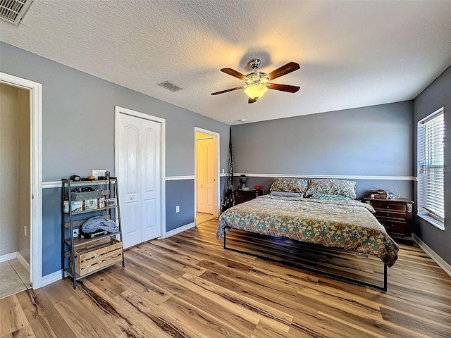 bedroom with ceiling fan, a textured ceiling, visible vents, and wood finished floors