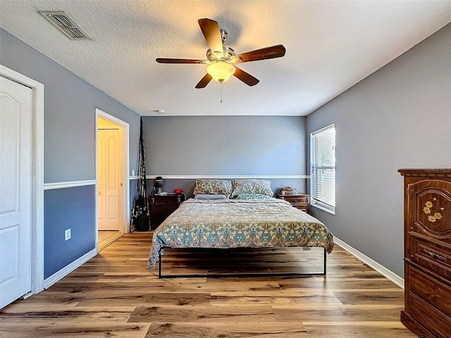 bedroom featuring baseboards, visible vents, ceiling fan, wood finished floors, and a textured ceiling