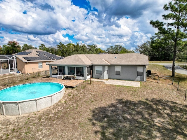 rear view of house with stucco siding, a sunroom, fence, an outdoor pool, and a wooden deck