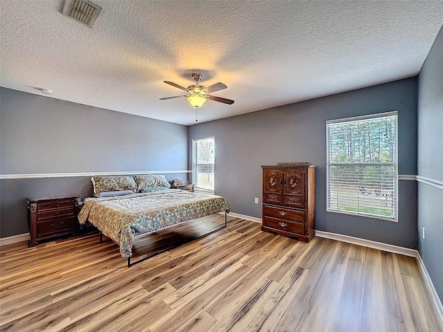 bedroom featuring visible vents, a ceiling fan, a textured ceiling, wood finished floors, and baseboards