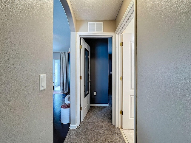 hall with arched walkways, a textured wall, a textured ceiling, visible vents, and carpet