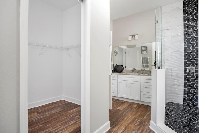 full bath with a walk in closet, wood finished floors, baseboards, tiled shower, and vanity
