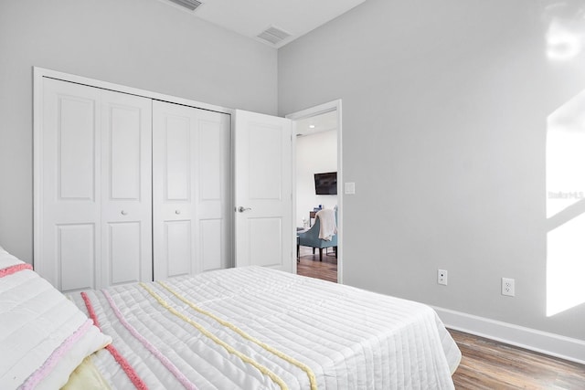 bedroom with wood finished floors, visible vents, a closet, and baseboards
