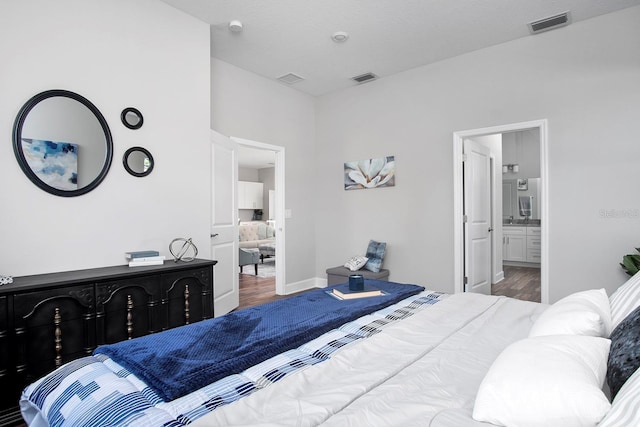 bedroom featuring visible vents, ensuite bath, baseboards, and wood finished floors