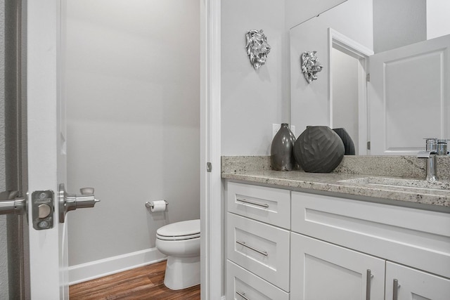 half bathroom with toilet, vanity, baseboards, and wood finished floors