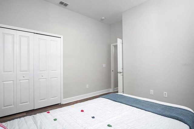 bedroom featuring wood finished floors, visible vents, baseboards, a closet, and a textured ceiling