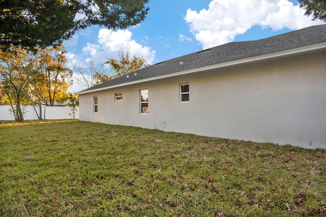 back of house featuring stucco siding, a lawn, and fence