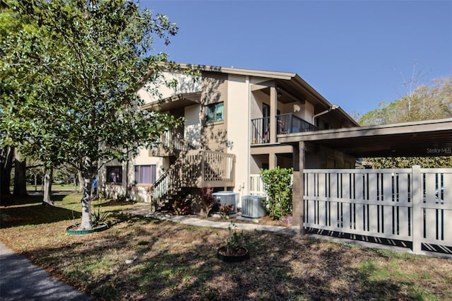 view of side of property featuring central air condition unit, fence, stucco siding, and stairway