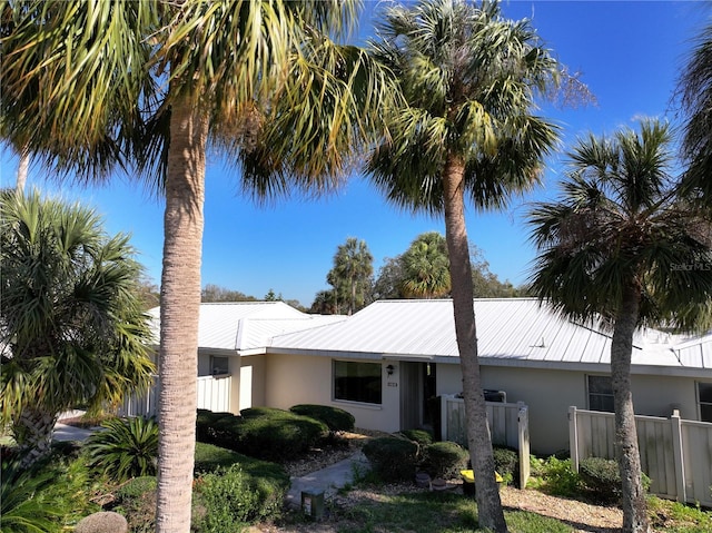 view of front of house featuring stucco siding, metal roof, and fence