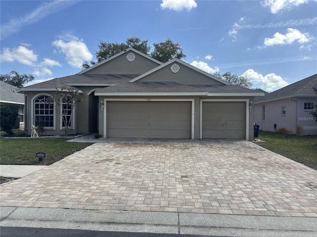 ranch-style house featuring a garage, stucco siding, roof with shingles, decorative driveway, and a front yard