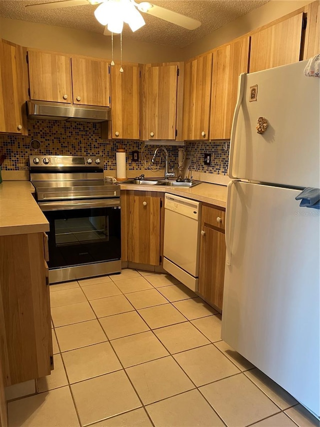 kitchen featuring a sink, tasteful backsplash, white appliances, light countertops, and under cabinet range hood