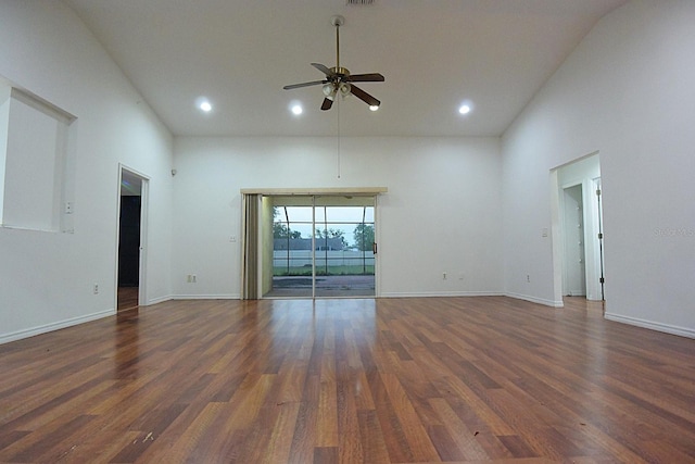 empty room with a ceiling fan, a towering ceiling, baseboards, and wood finished floors