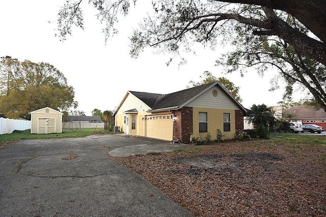 view of side of home with aphalt driveway, brick siding, a storage shed, fence, and a garage