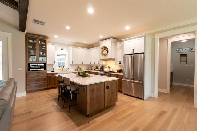 kitchen featuring visible vents, a center island, a kitchen breakfast bar, high quality fridge, and white cabinetry