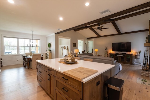 kitchen featuring visible vents, brown cabinets, lofted ceiling with beams, a kitchen island, and light wood finished floors