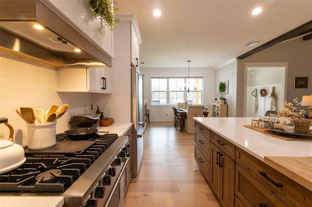 kitchen with light wood finished floors, stainless steel appliances, light countertops, white cabinets, and wall chimney range hood