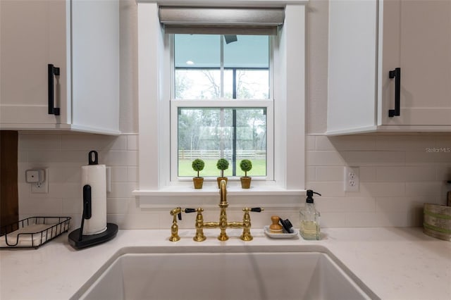 interior details with white cabinetry, light countertops, backsplash, and a sink