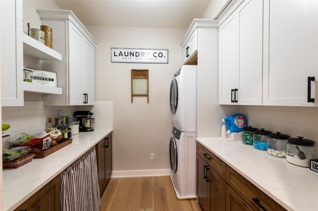 laundry room featuring baseboards, cabinet space, light wood-style flooring, and stacked washer / dryer