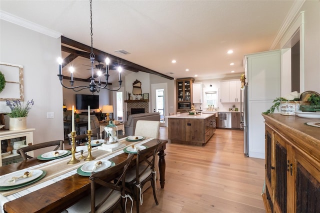 dining area featuring visible vents, a notable chandelier, ornamental molding, a fireplace, and light wood finished floors