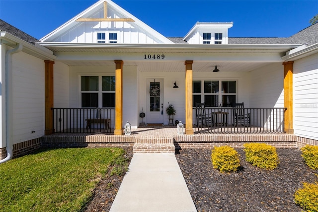 entrance to property featuring a porch, a shingled roof, and board and batten siding