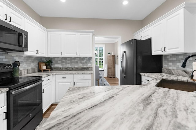 kitchen featuring light stone counters, freestanding refrigerator, a sink, stainless steel microwave, and black electric range oven