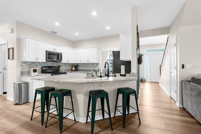 kitchen with stainless steel microwave, a breakfast bar area, freestanding refrigerator, black electric range, and white cabinets