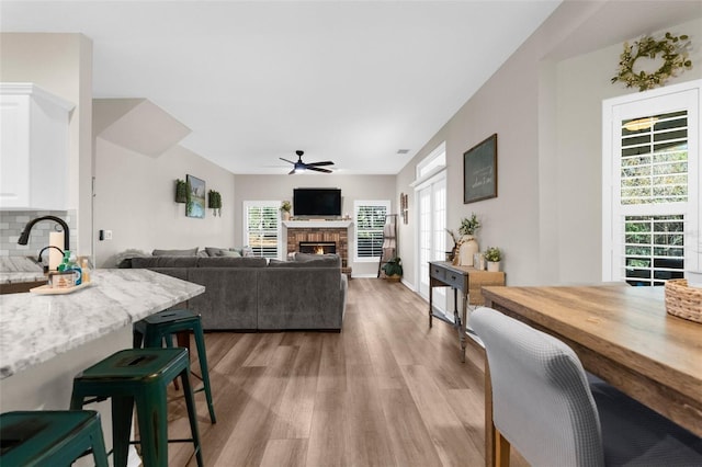 dining area with a ceiling fan, wood finished floors, and a warm lit fireplace