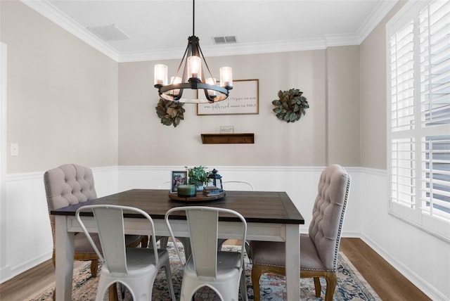 dining area featuring visible vents, a chandelier, ornamental molding, wainscoting, and wood finished floors