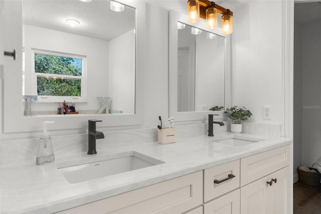 bathroom with double vanity, wood finished floors, a textured ceiling, and a sink