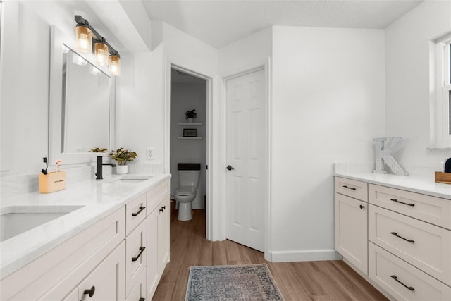 full bathroom with toilet, a sink, wood finished floors, double vanity, and baseboards