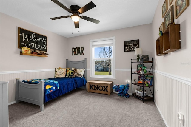 carpeted bedroom featuring wainscoting and a ceiling fan