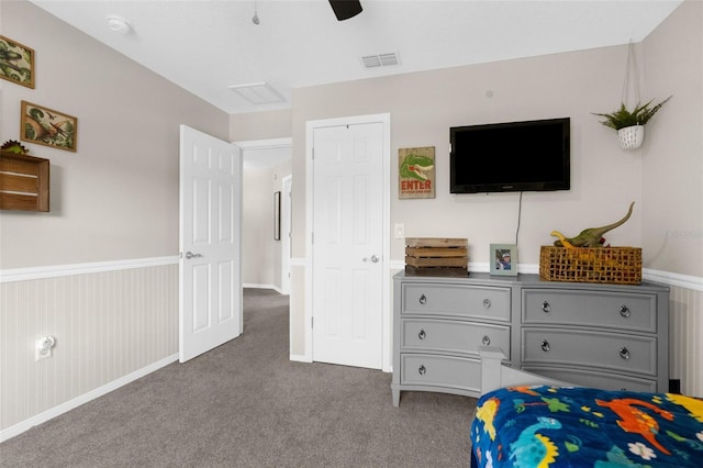 bedroom with a wainscoted wall, visible vents, carpet floors, and ceiling fan