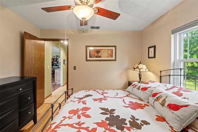 bedroom featuring visible vents, ceiling fan, a textured ceiling, and light wood-style floors