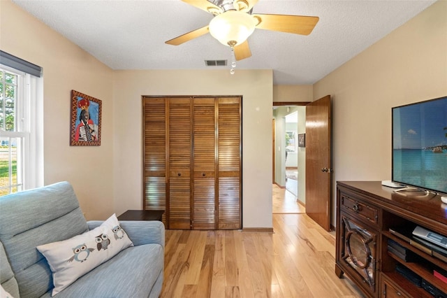 sitting room with visible vents, light wood-style flooring, a textured ceiling, and ceiling fan