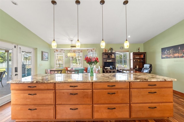 kitchen featuring lofted ceiling, light stone counters, wood finished floors, and pendant lighting