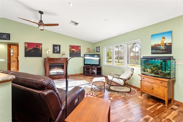 living room featuring visible vents, a glass covered fireplace, wood finished floors, baseboards, and vaulted ceiling