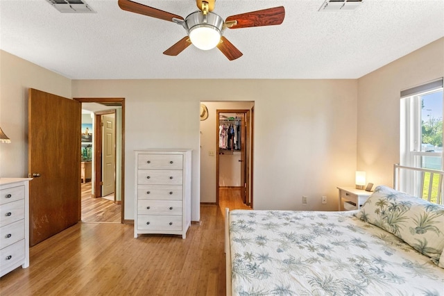 bedroom featuring a walk in closet, a textured ceiling, visible vents, and light wood-type flooring