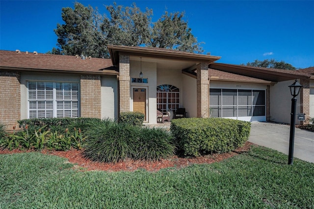 view of front facade featuring brick siding, a shingled roof, concrete driveway, a front yard, and a garage