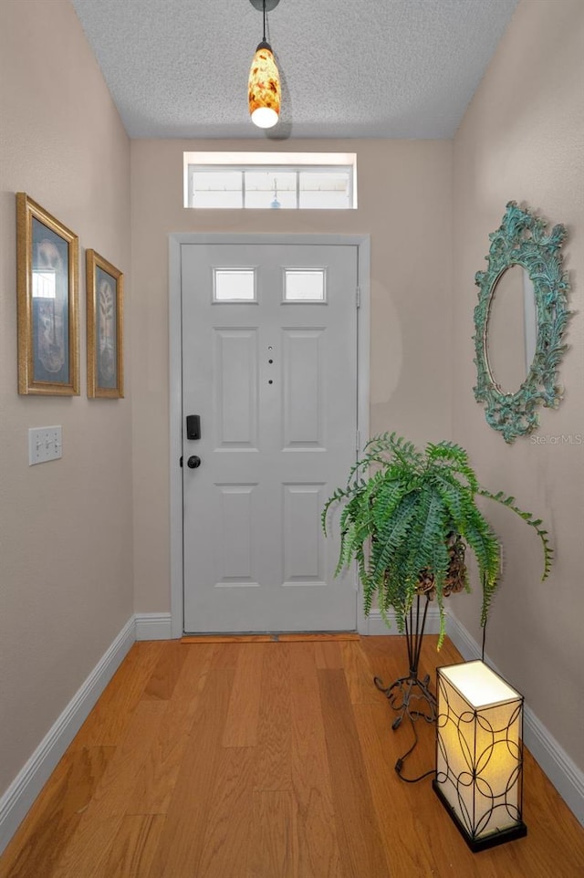 foyer with baseboards, light wood-type flooring, and a textured ceiling