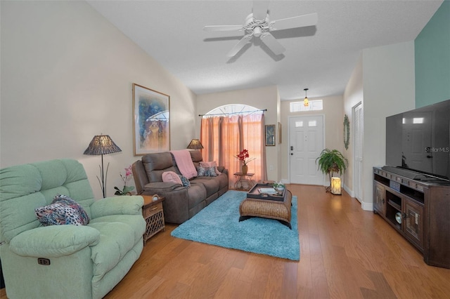 living area featuring baseboards, lofted ceiling, wood finished floors, and a ceiling fan