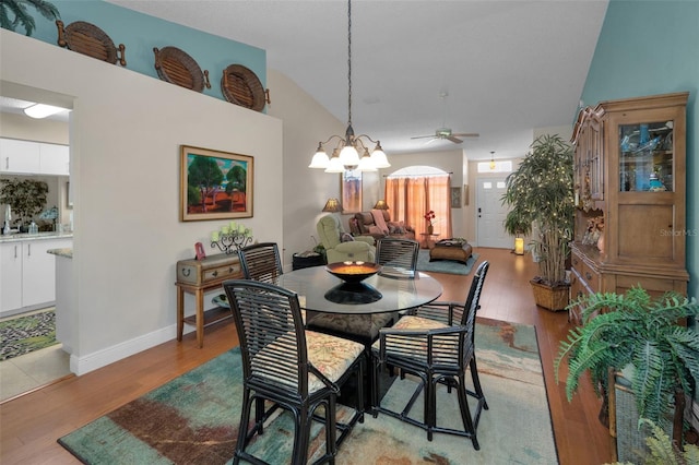 dining room featuring lofted ceiling, light wood-style flooring, ceiling fan with notable chandelier, and baseboards