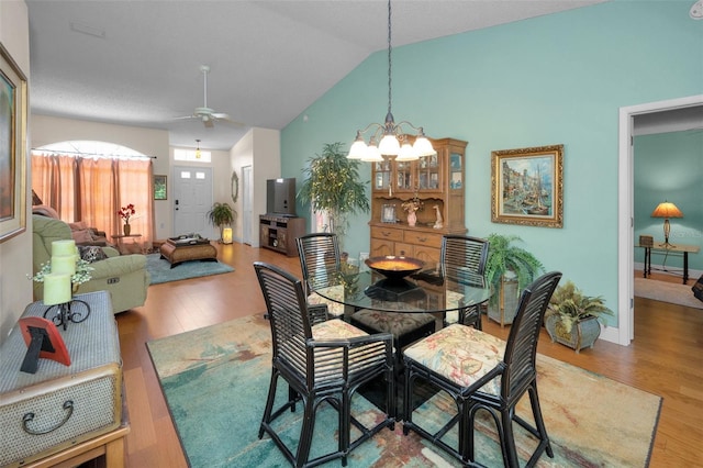 dining space featuring baseboards, ceiling fan with notable chandelier, wood finished floors, and vaulted ceiling