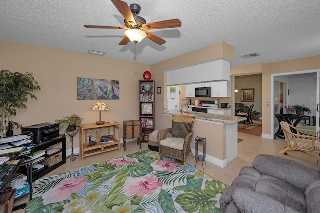 living area featuring visible vents, baseboards, a textured ceiling, and ceiling fan