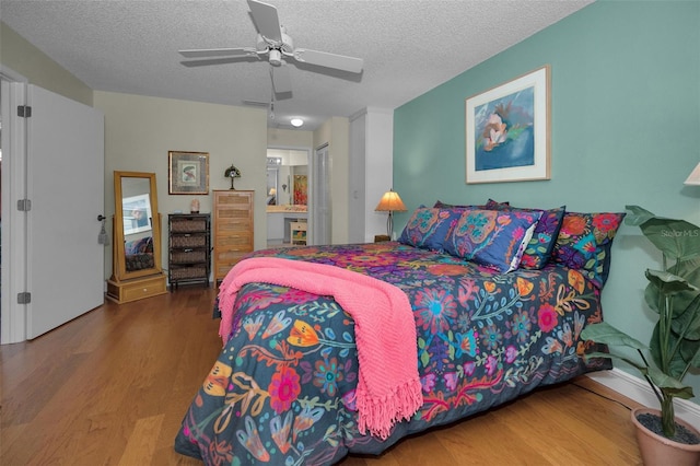 bedroom with a ceiling fan, a textured ceiling, ensuite bath, wood finished floors, and a closet